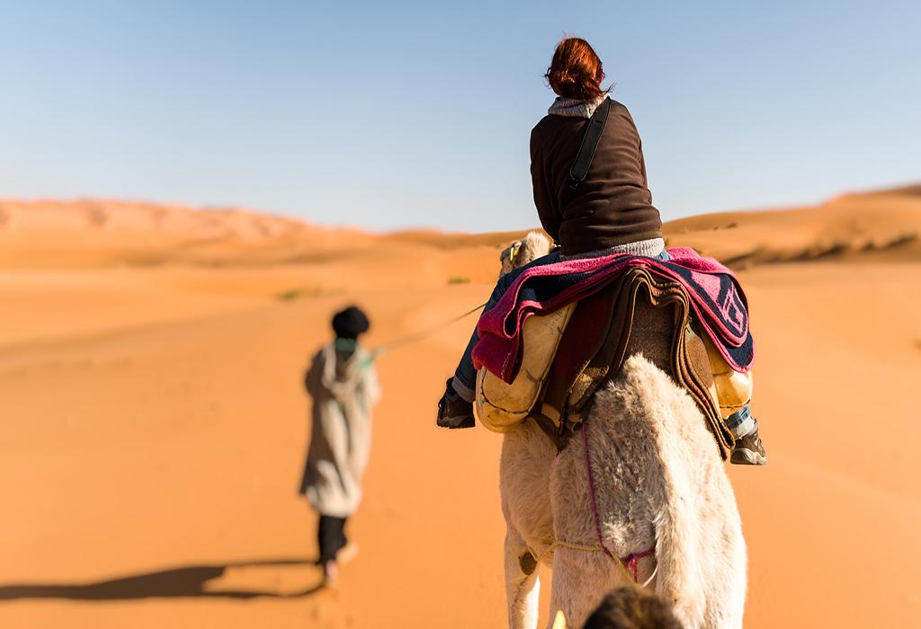Woman traveling on camel led by a berber nomad, back view